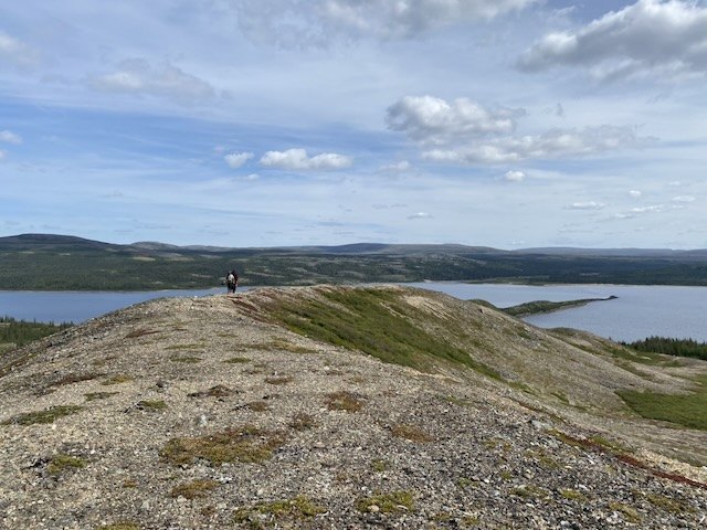 Une personne marche sur la crête de l’esker de la Pointe Wedge, couverte de lichens et de cailloux, qui s’avance dans la rivière George