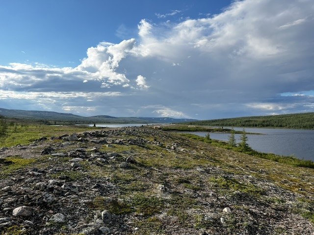Une terrasse pierreuse couverte de mousses descend vers le lac, sous de grands cumulus